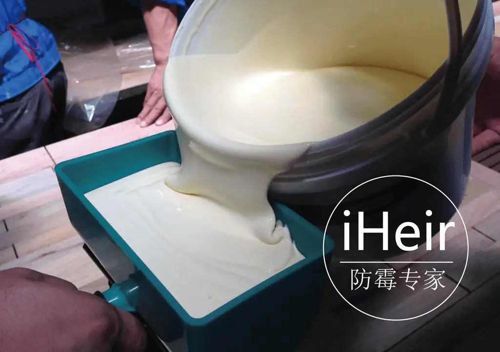 工人将乳白色涂料倒入托盘的调漆作业现场