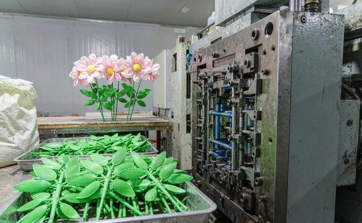 Injection-moulded artificial flower stems and leaves: freshly moulded green plastic parts beside silk flowers