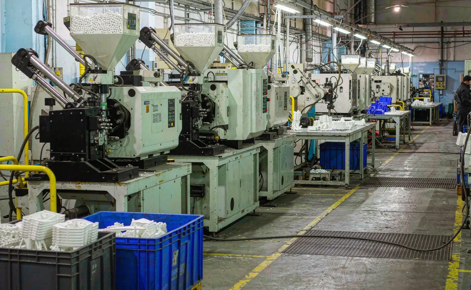 Injection moulding workshop: rows of moulding machines with hoppers, blue crates of freshly moulded white plastic parts