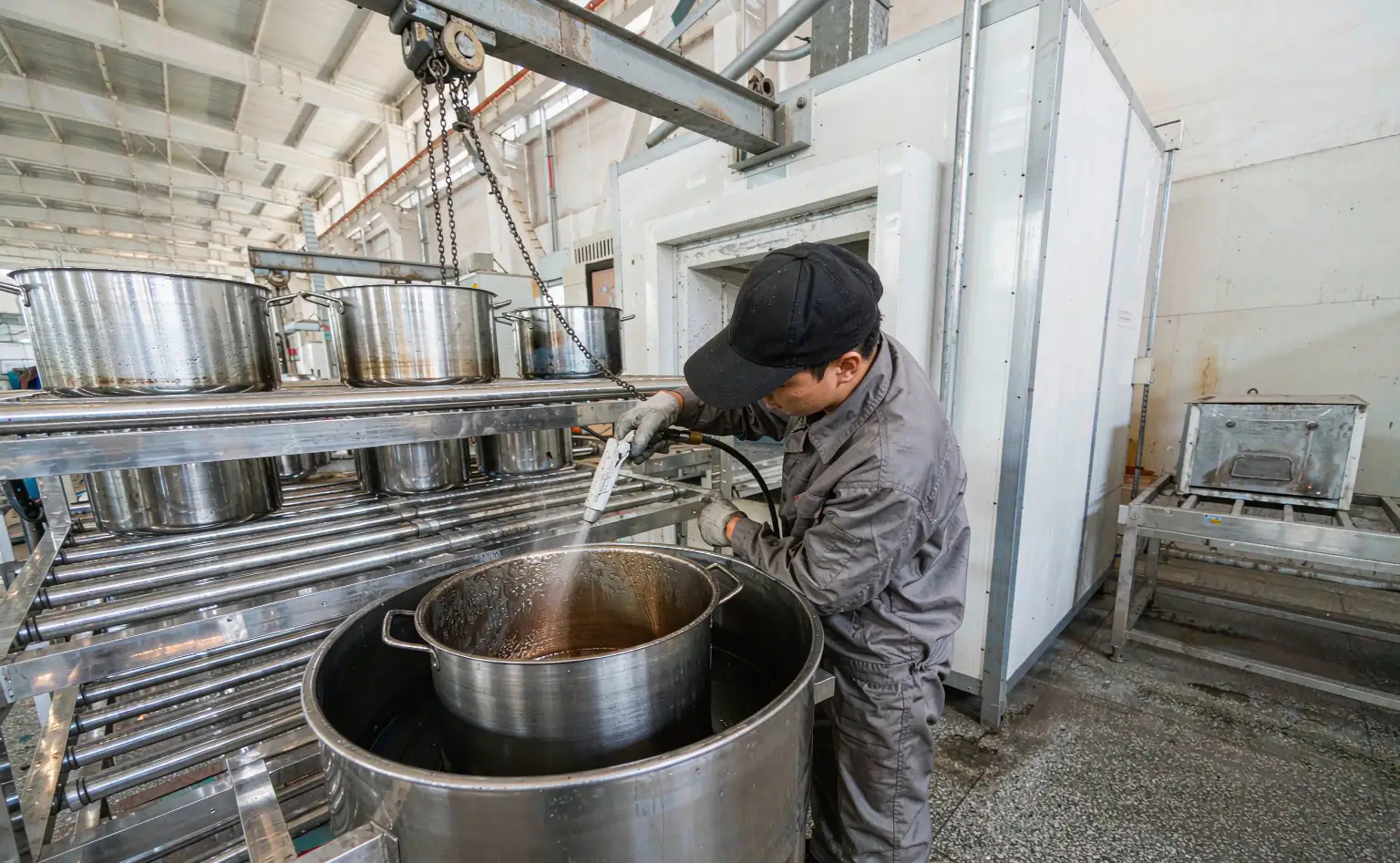 内胆喷涂线：工人手持喷枪给不锈钢内胆喷涂涂层，传送带通向烘干炉