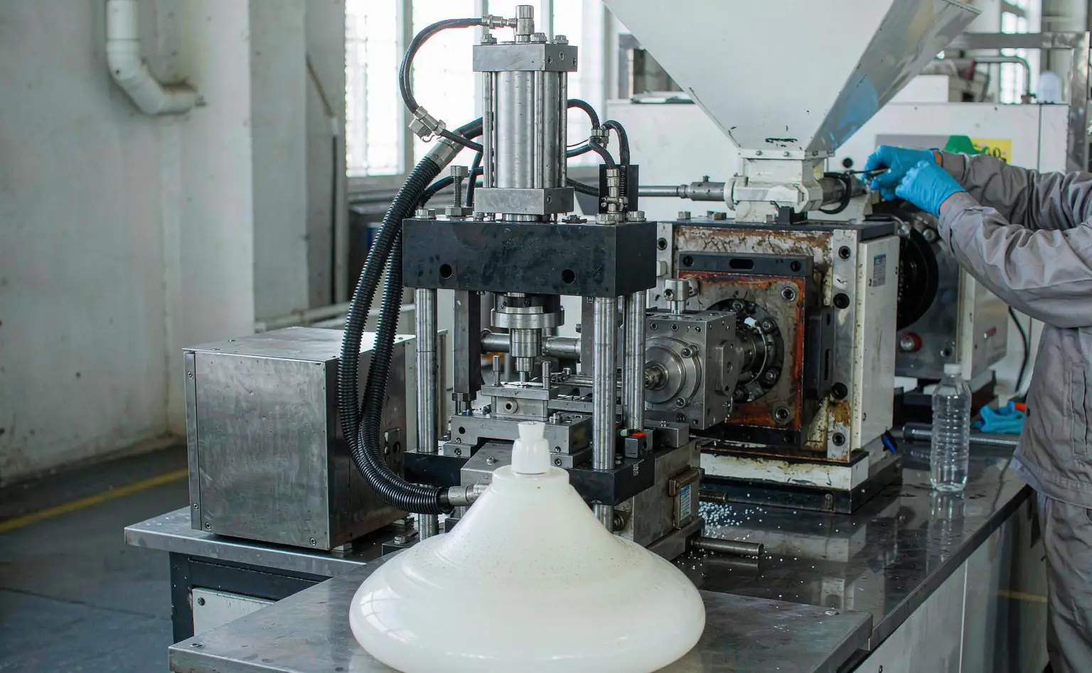 Plastic moulding shop: cream-coloured lamp shades just ejected from an injection moulding machine, with an operator in gloves loading material at the hopper
