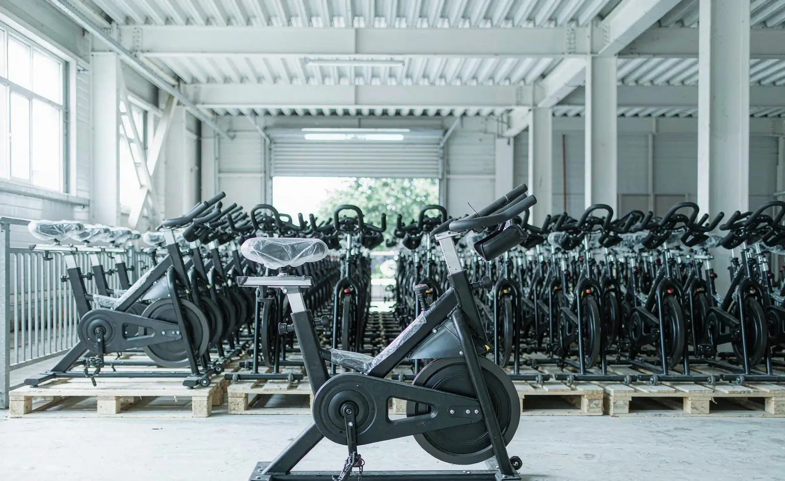 Finished-goods store: assembled spin bikes parked in rows with the frame coating intact, saddles under dust covers and pallets on the floor