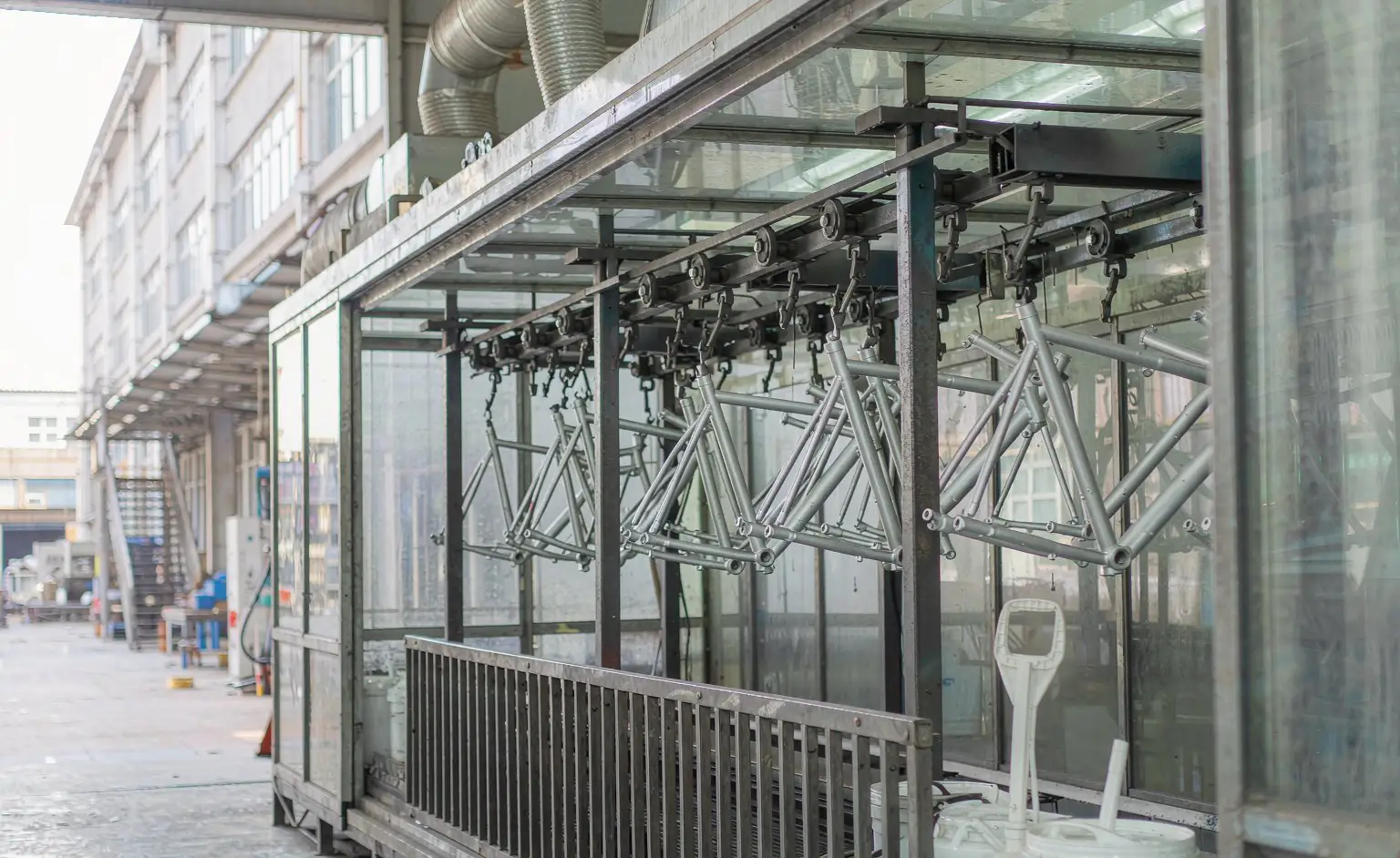 Coating line: bike frames travelling through the spray booth on the overhead conveyor, paint mixing pails and a stirrer beside the booth