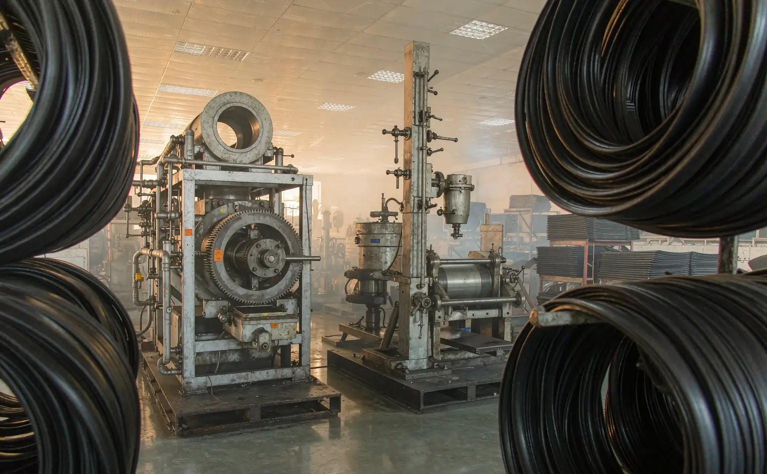 Gasket area: coils of black sealing strip hanging on a rack beside an internal mixer and a two-roll mill, with sheeted compound stacked on pallets