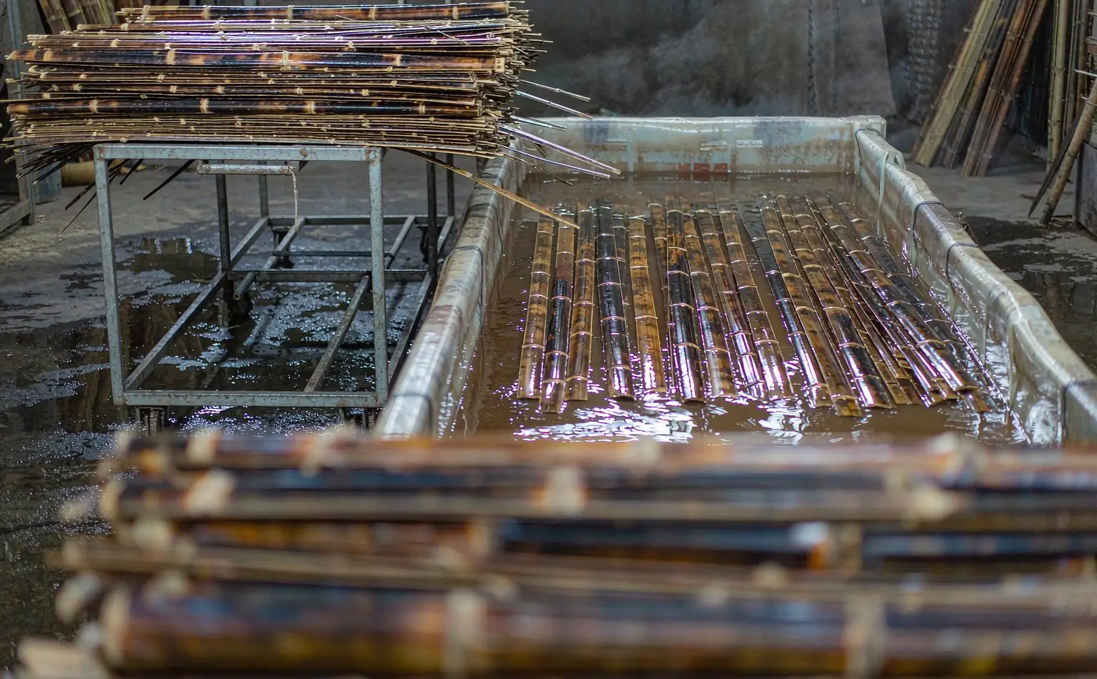 Carbonisation and dip area: carbonised bamboo strips stacked on a trolley beside a rectangular dip tank, bundles fully submerged