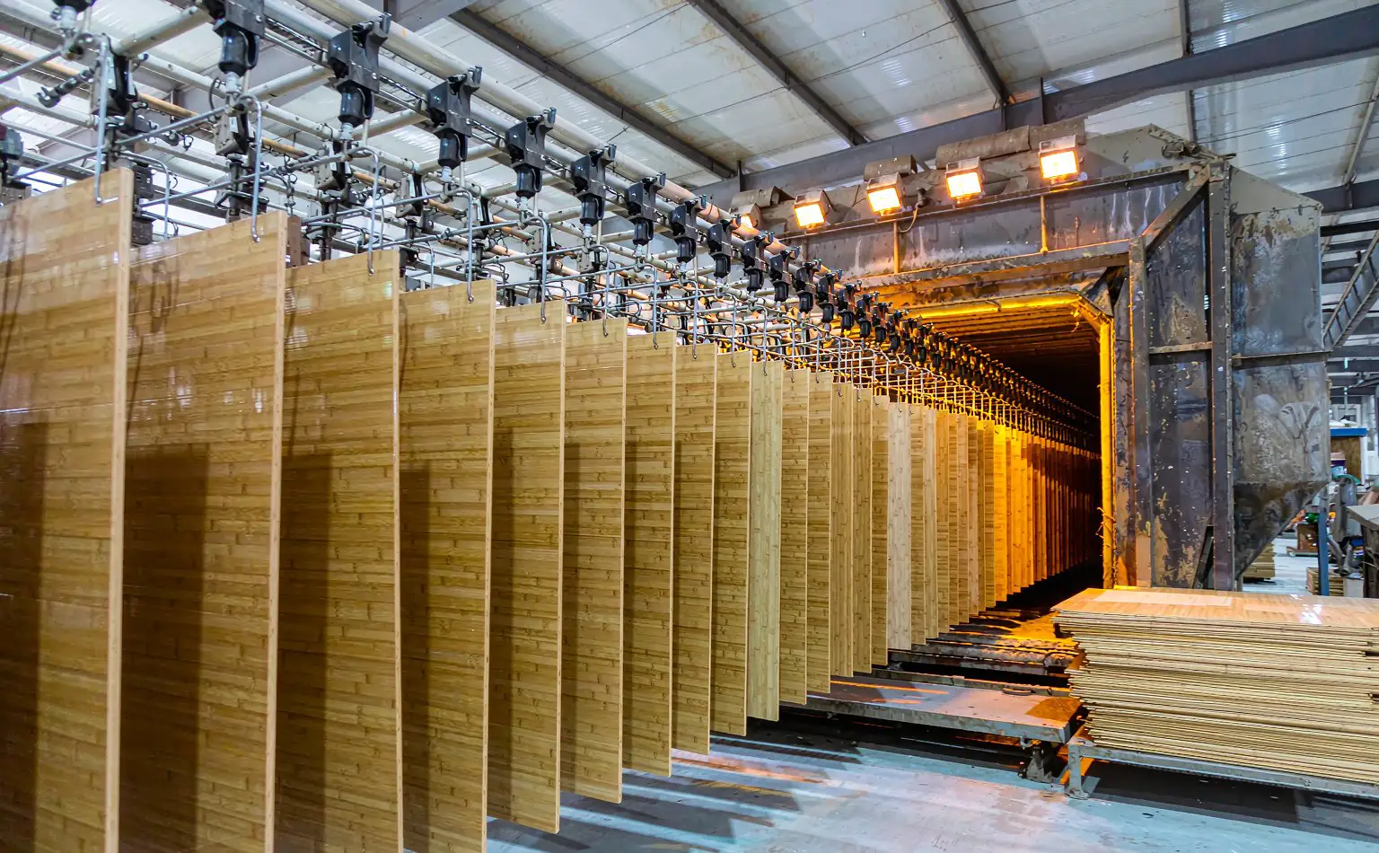 Bamboo flooring shop: flooring boards travelling on the coating line hangers towards the drying tunnel, with finished stacks beyond