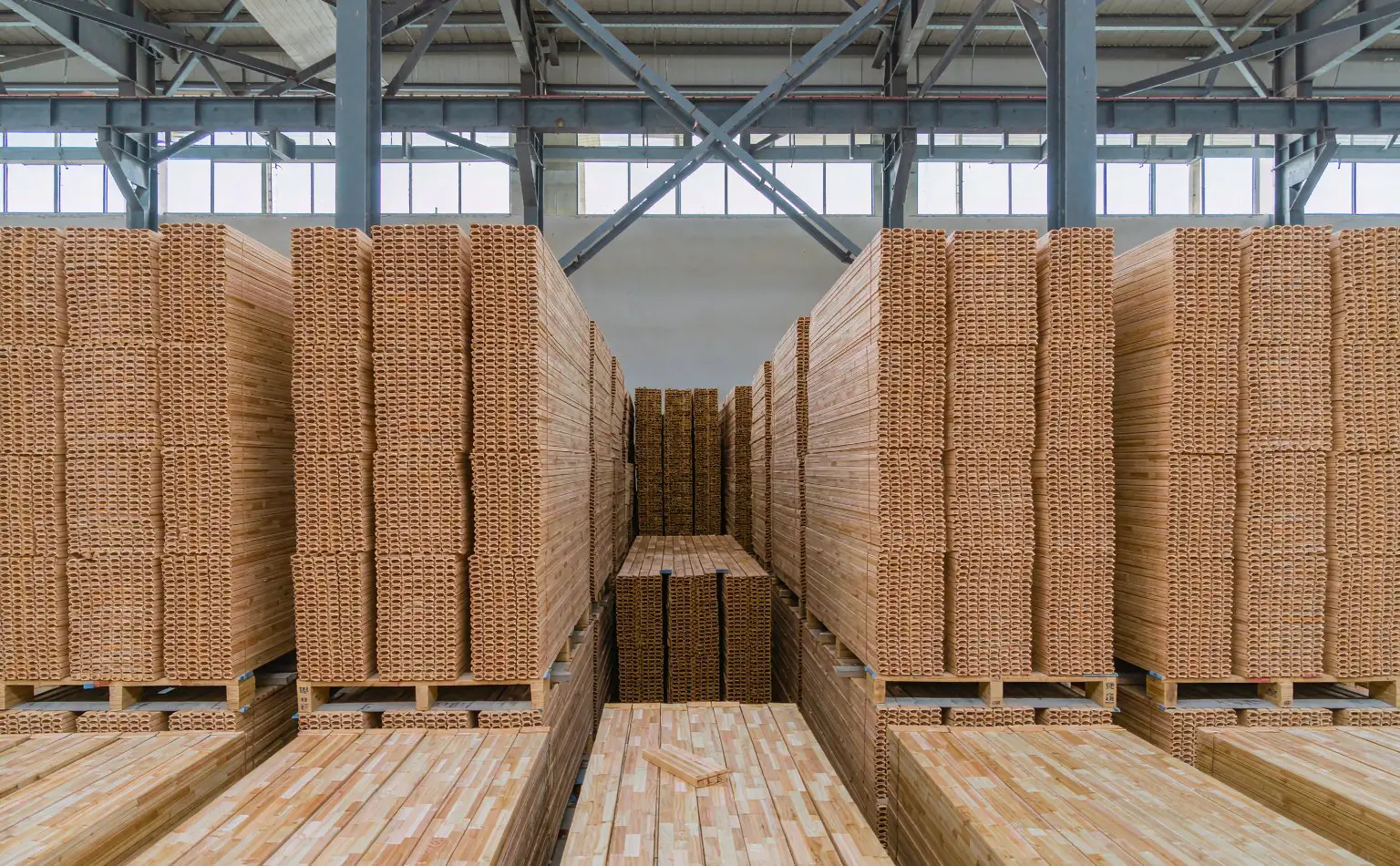 Finished-goods store: stacks of bamboo flooring with the cut ends facing out, timber pallets underneath and steel roof beams above