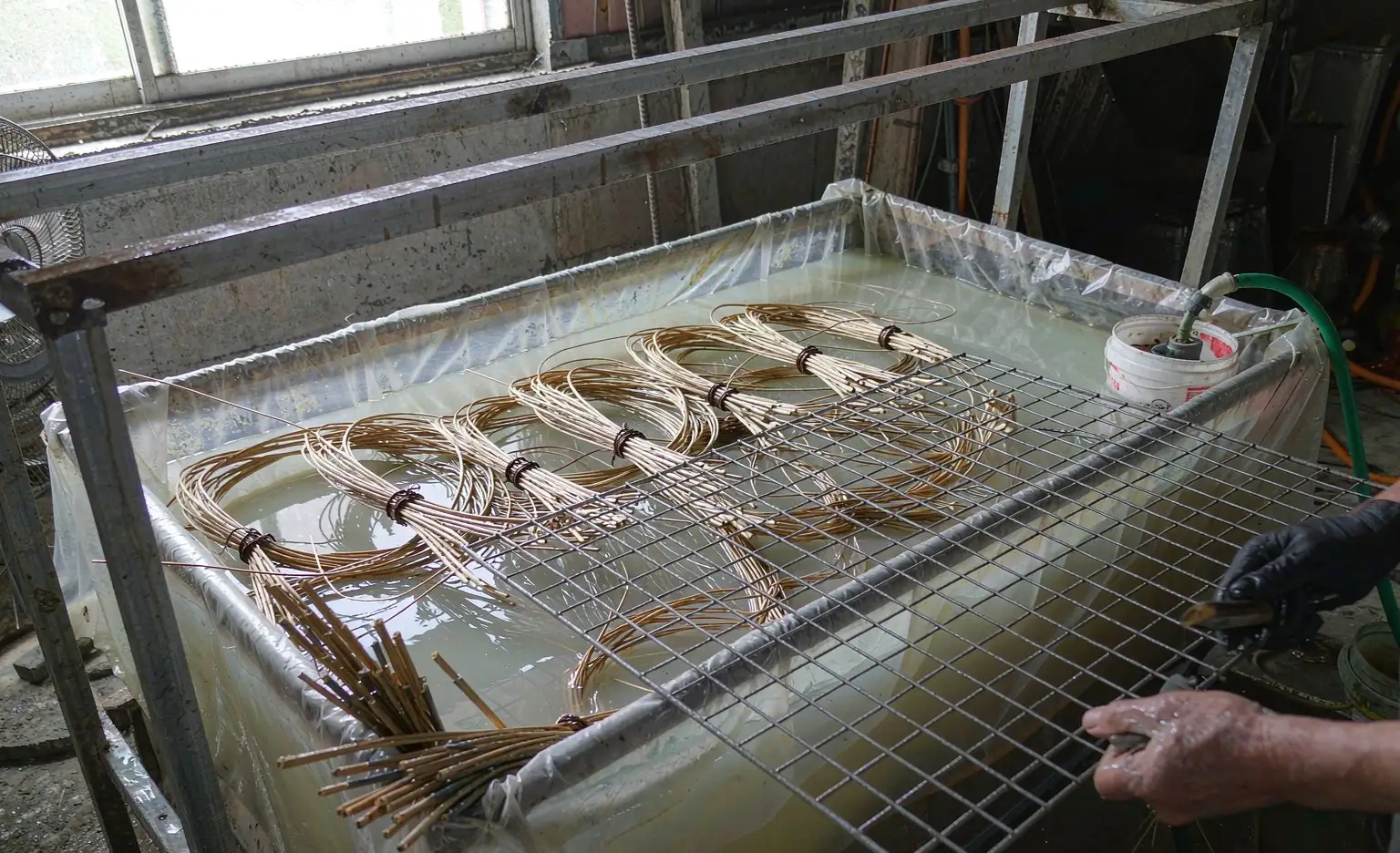 藤条浸泡区：成捆藤条浸在长方形塑料槽里，槽边放着沥水架与周转筐
