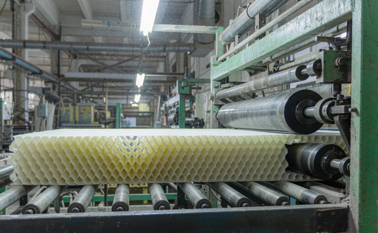 Honeycomb board line: the stretched paper core runs forward as hexagonal cells while the top and bottom facing sheets are pressed on at the combining rolls