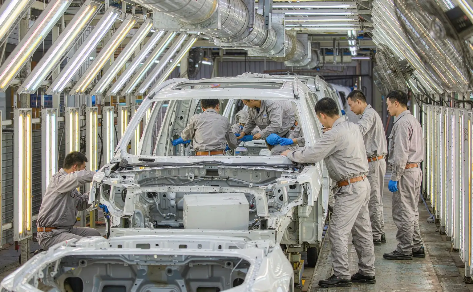 Vehicle assembly line: workers fitting the dashboard module into the body at a lit station