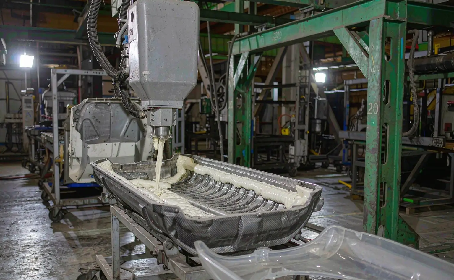 Dashboard foaming line: a mixing head pouring foam into an open dashboard mould, the foam layer forming in the cavity