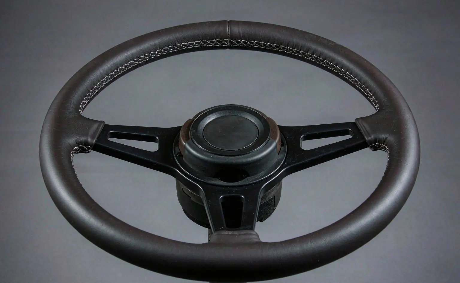Finished steering wheel: a three-spoke leather-wrapped wheel with visible stitching on a grey background