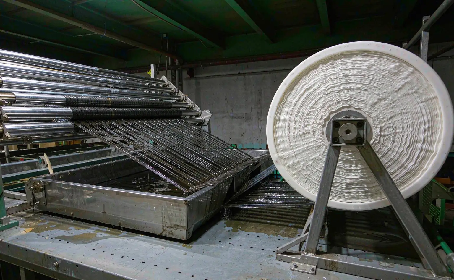 Webbing padding line: dark polyester webbing running through a padding trough of treatment liquid and squeeze rollers, a mixing pail beside the trough