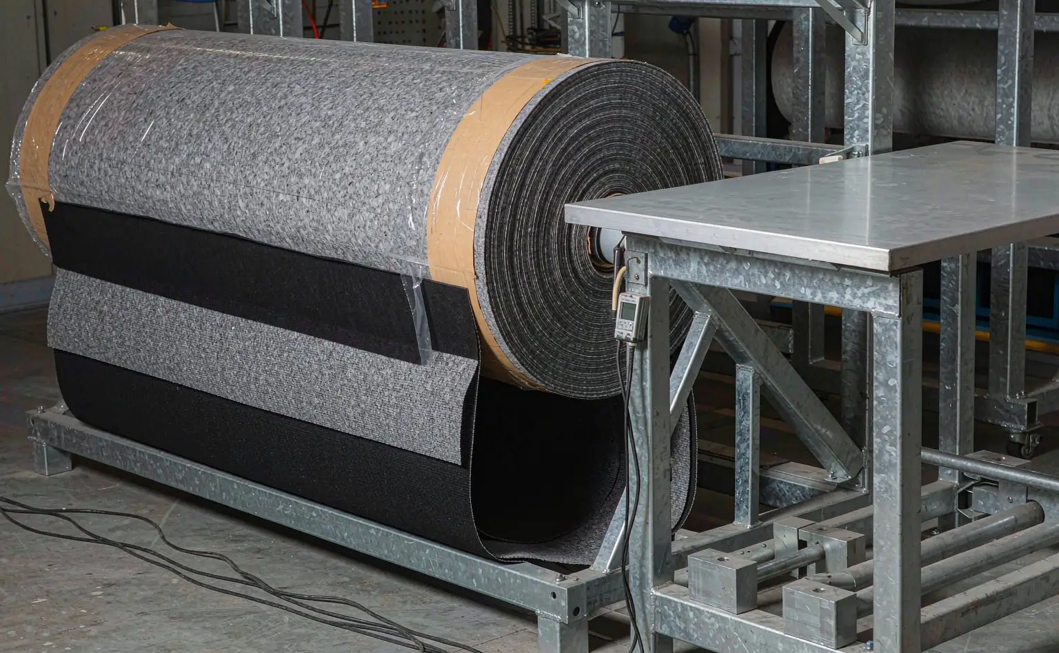 Nonwoven roll store: vertical rolls of grey-white nonwoven and knit composite fabric racked on shelves with aisle markings on the floor