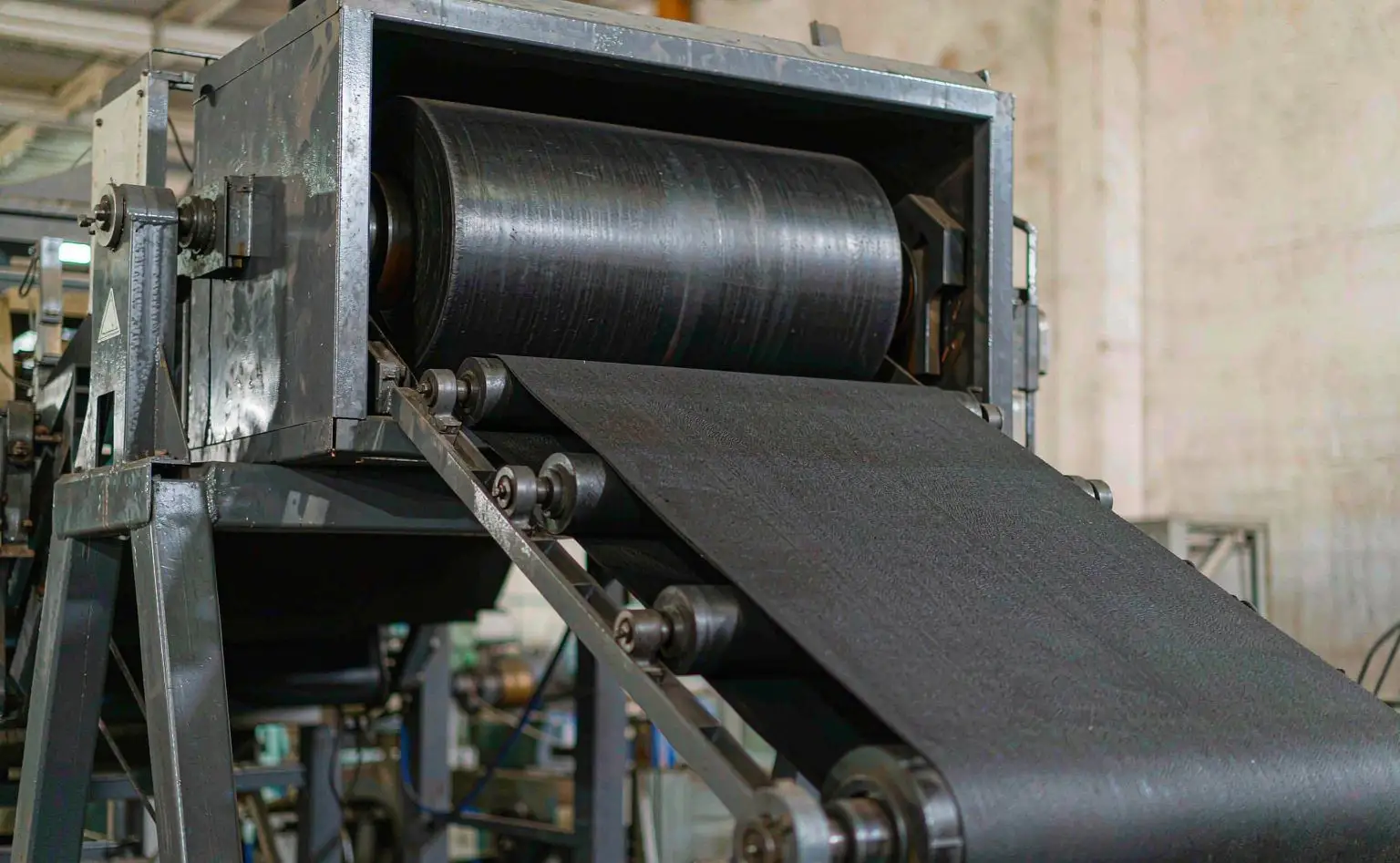 Foam line: black rubber-plastic foam sheet emerging continuously from the foaming oven with a fine cell structure, wound onto a roller at the end