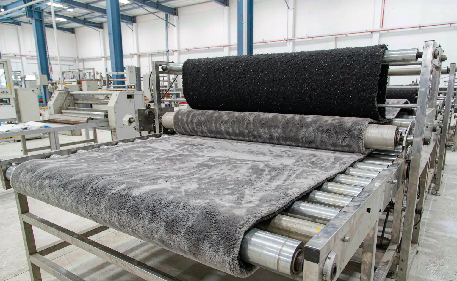 Laminating shop: grey suede-like fabric feeding through laminating rollers with the foam backing, the finished composite leaving as a full sheet