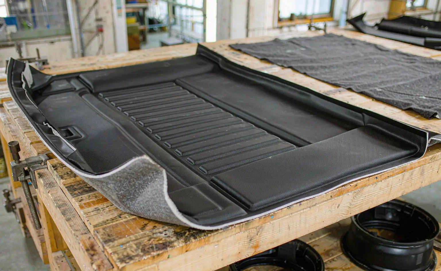 Automotive trim shop: a shaped black trunk mat lying flat on a workbench, its edges neatly bonded and a non-slip pattern on the face