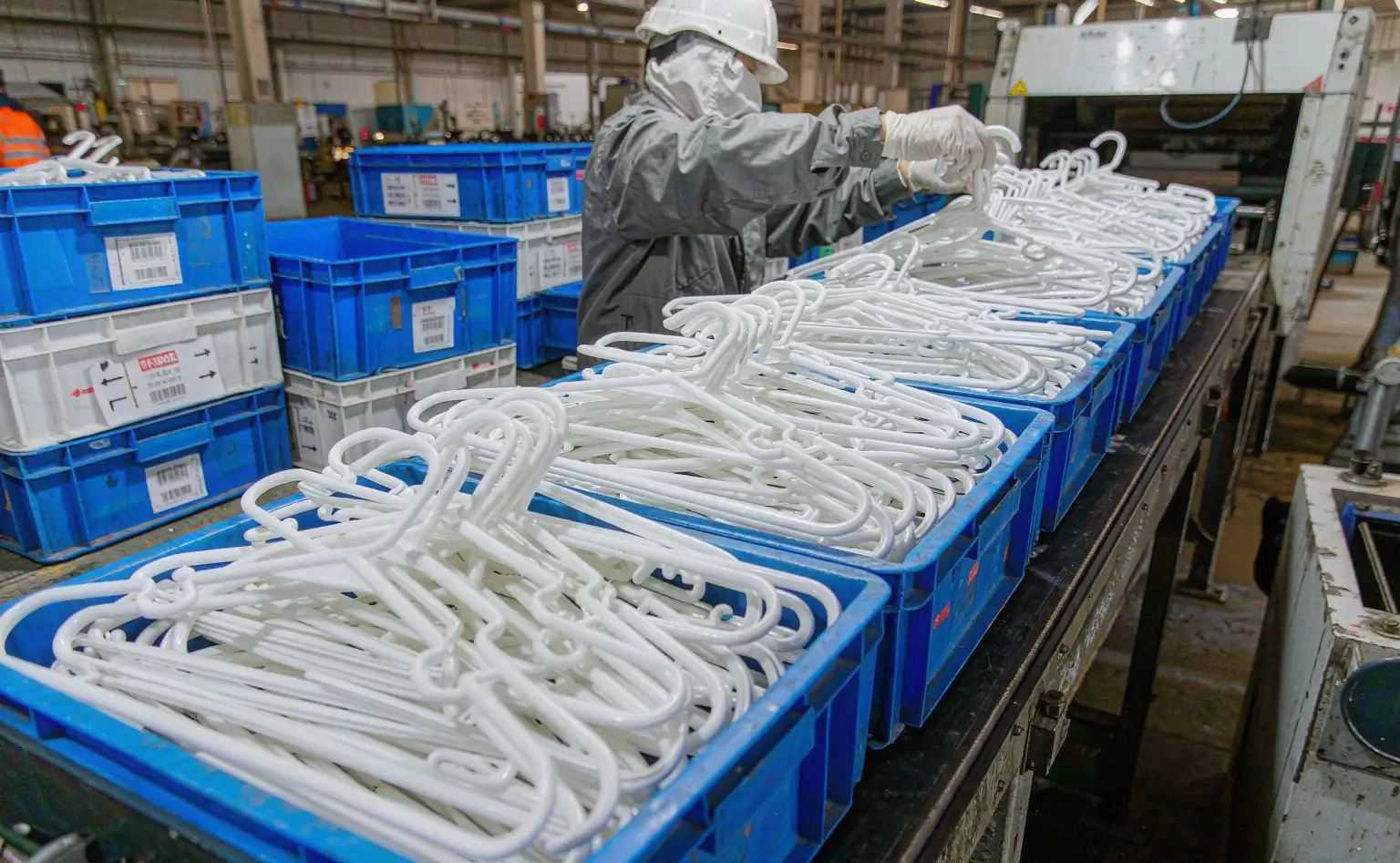 成品筐工位：蓝色塑料筐里码满刚下线的衣架，工人戴手套分拣，旁边摆着贴好标签的周转箱