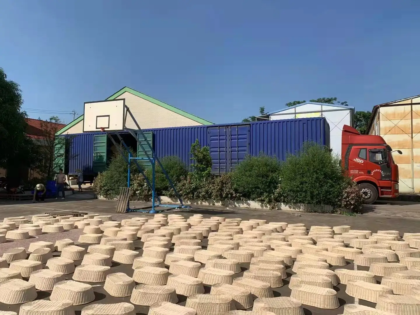 厂区晾晒：大量的竹蒸笼摊在室外水泥地上晾晒，蒸笼圈口朝上，背景是厂房与货柜