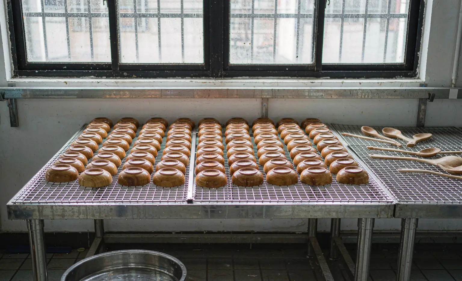 晾干架：浸过的木碗倒扣在不锈钢晾干架上，木勺平铺在旁边的网架上，地面有接水盘